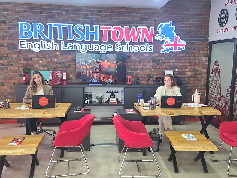 British Town Döşemealtı karşılama alanı, danışman masaları ve tuğla duvar logosu